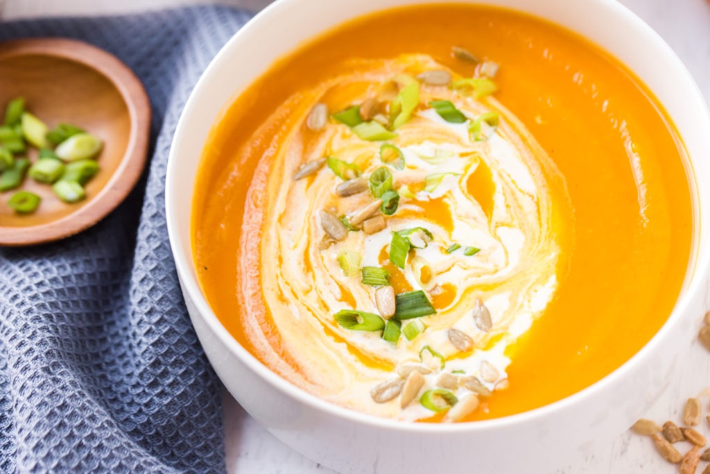 Butternut squash soup in a bowl topped with half and half, chopped scallions and sunflowers 