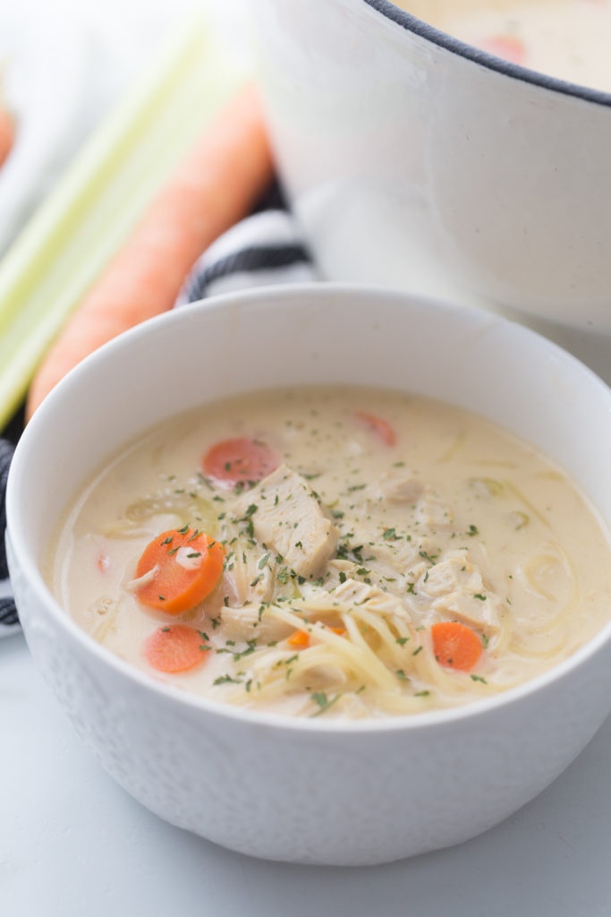 creamy chicken noodle soup in a white bowl, next to a pot of soup