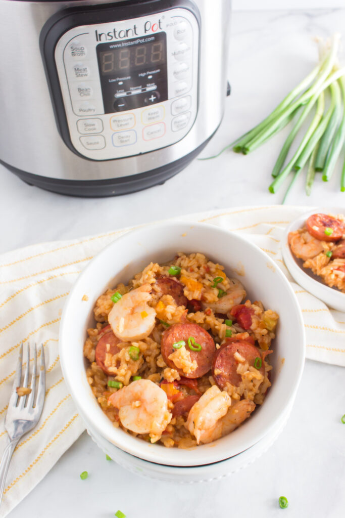 Jambalaya in a white bowl with pressure cooker in the background.