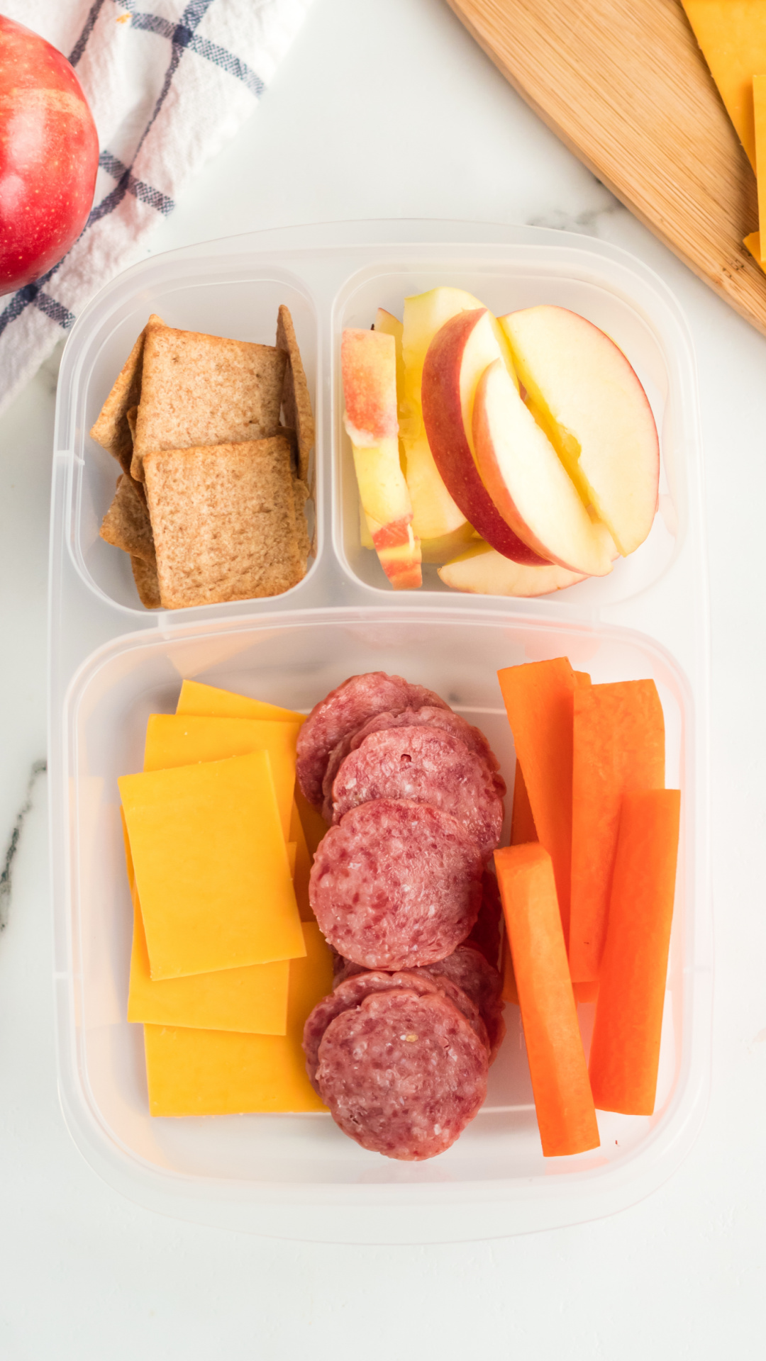lunch box with sliced ​​cheese, salami, carrots, apples and crackers