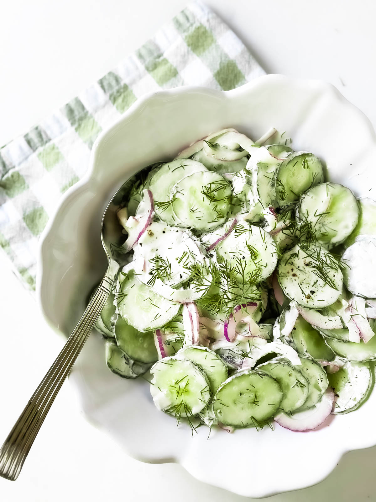Classic cucumber salad in a white bowl with a checkered napkin.