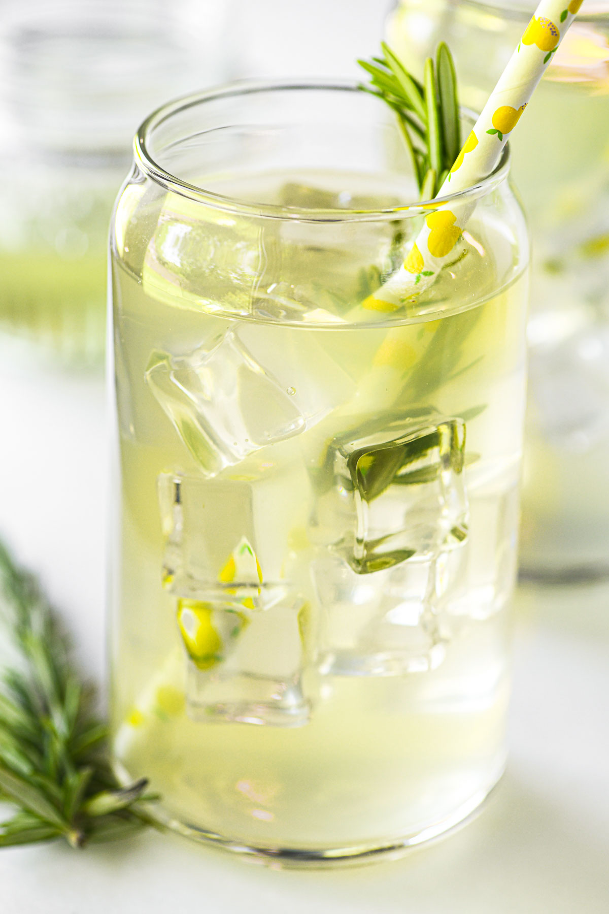 A glass of rosemary lemonade with sprigs of fresh rosemary.
