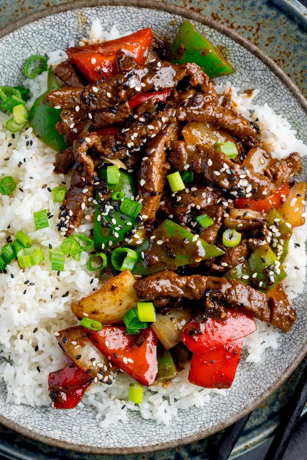 Beef in black bean sauce stir-fried with boiled rice in a bowl, topped with scallions and sesame seeds.