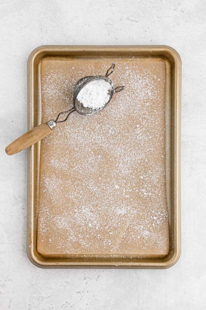 Powdered sugar being sprinkled on parchment paper