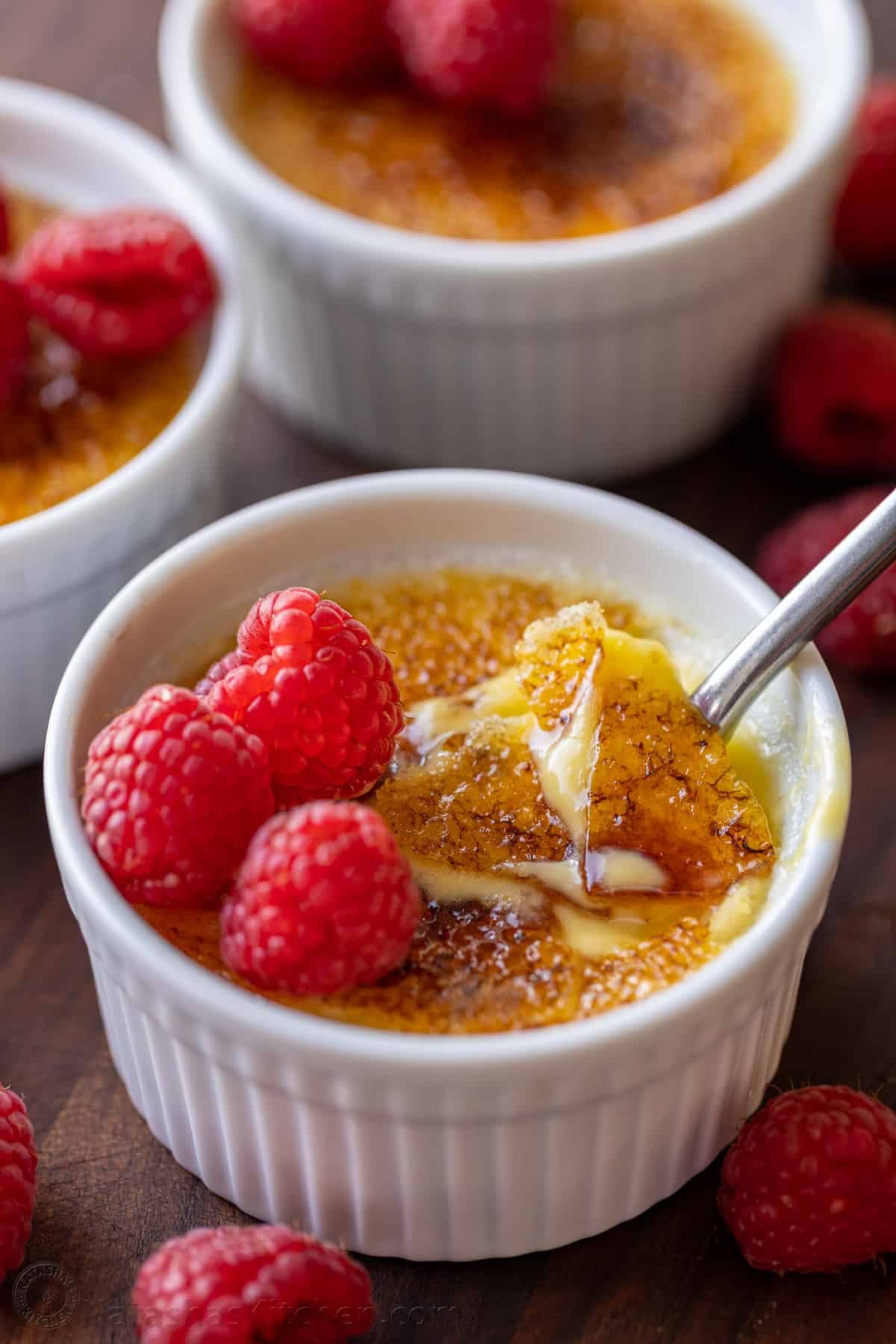 Creme brulee topped with raspberries, with the caramelized sugar topping cracked with a spoon.
