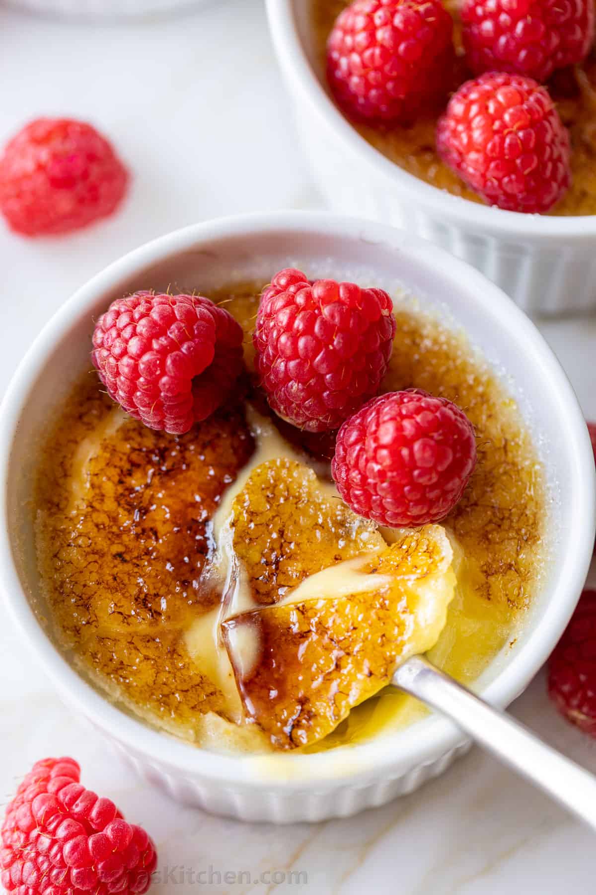 Overhead view of creme brulee topped with raspberries, with the caramelized sugar topping cracked with a spoon.