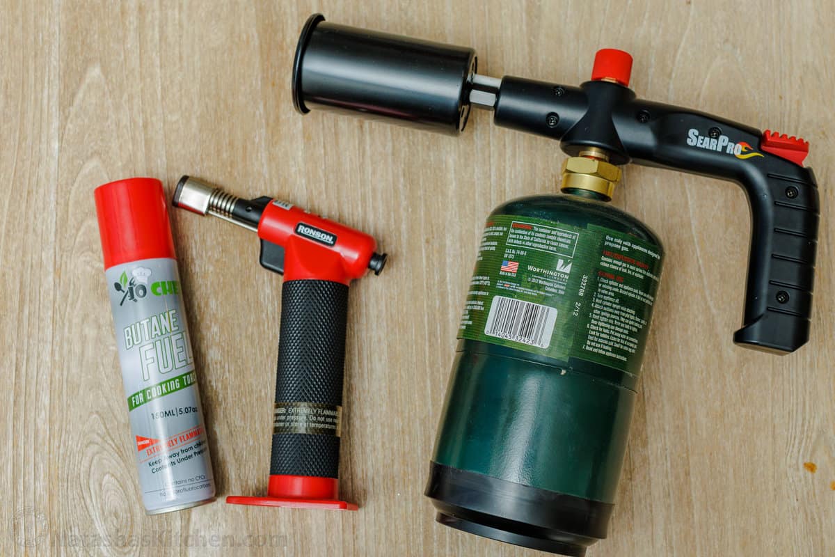 Overhead view of large and small kitchen torches on a countertop next to a can of butane.