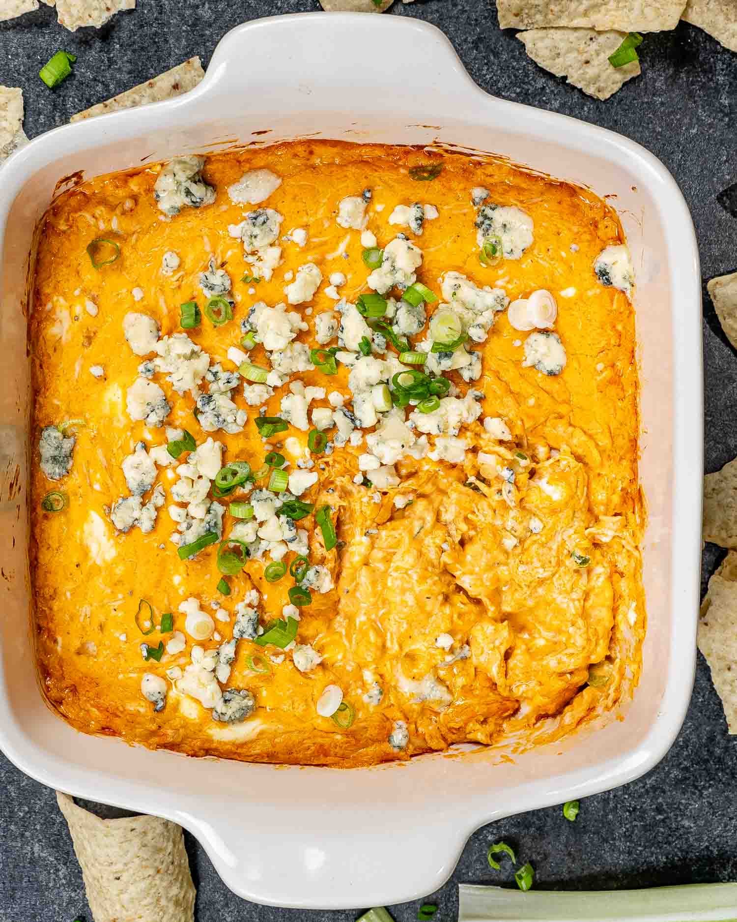 buffalo chicken sauce in a square baking dish garnished with blue cheese and green onions.