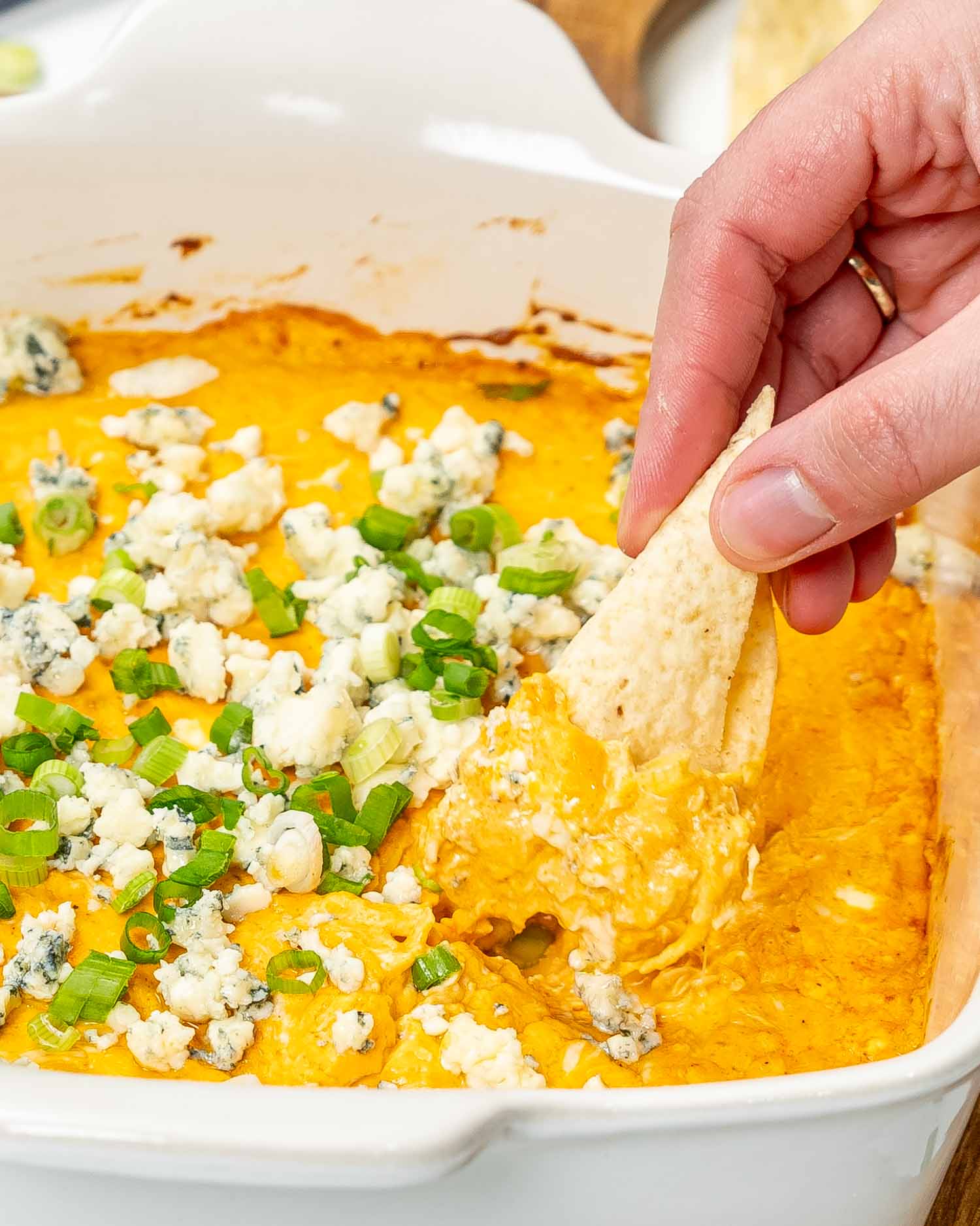 buffalo chicken sauce in a square baking dish garnished with blue cheese and green onions.