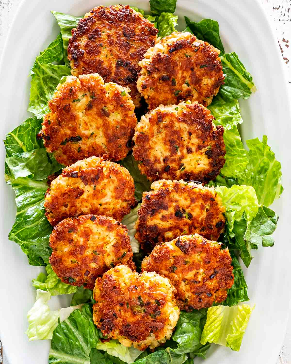 a few crab cakes on a bed of lettuce on a white platter.