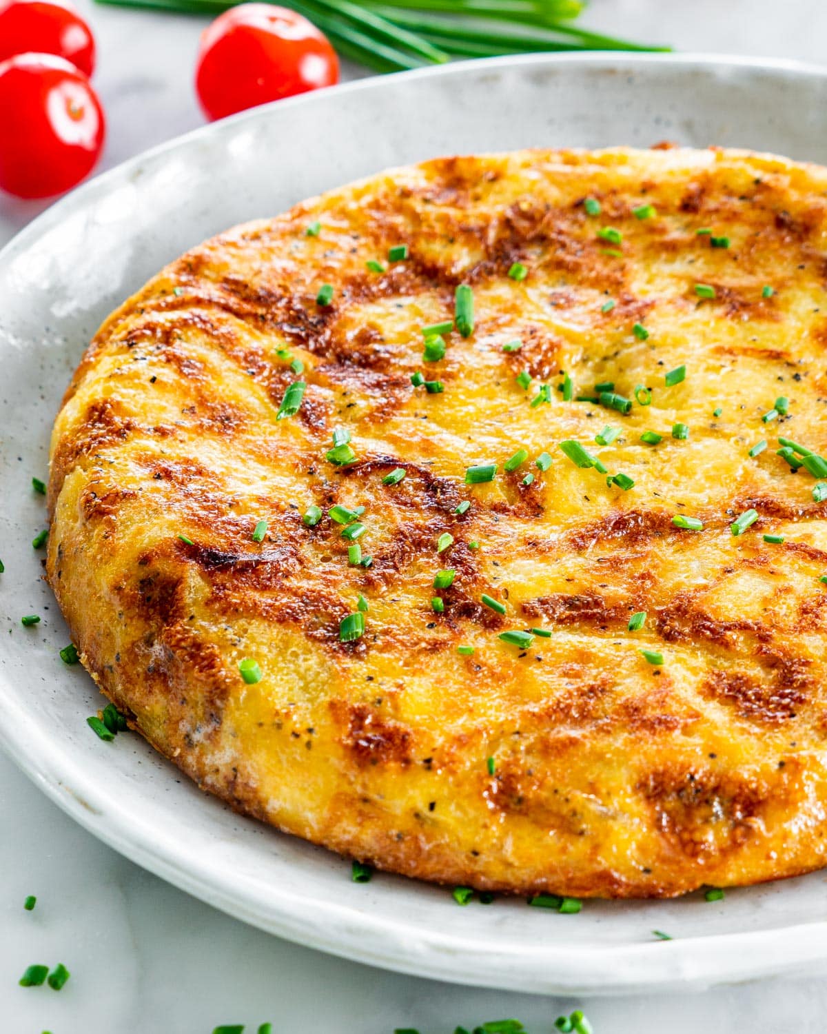 Side view of a complete Spanish tortilla on a gray plate garnished with chives
