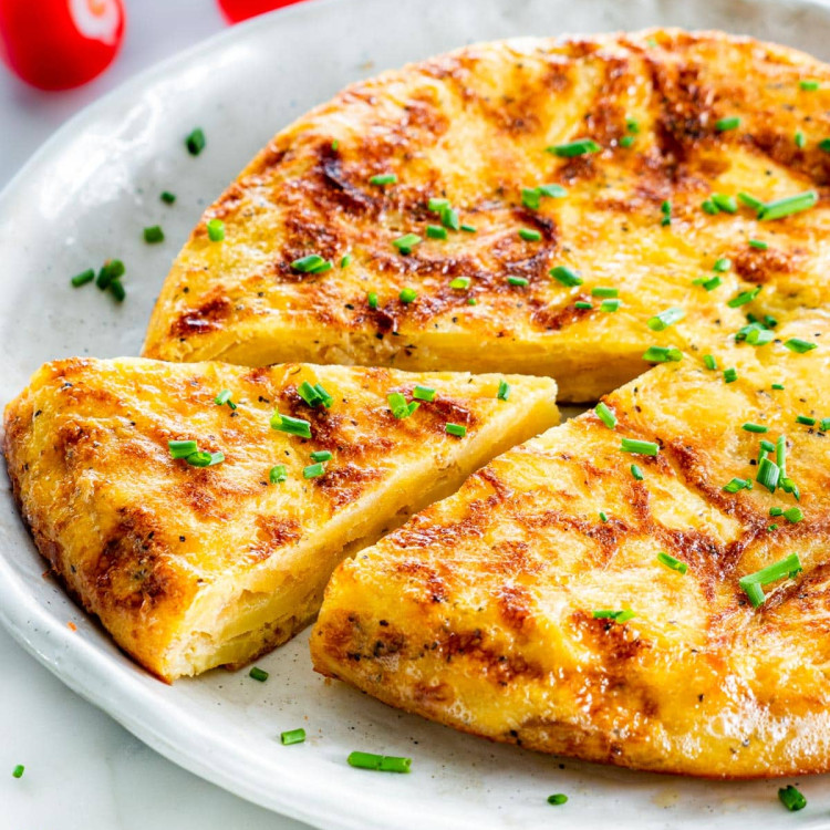 Side view of Spanish tortilla on a plate with one slice cut out and garnished with chives