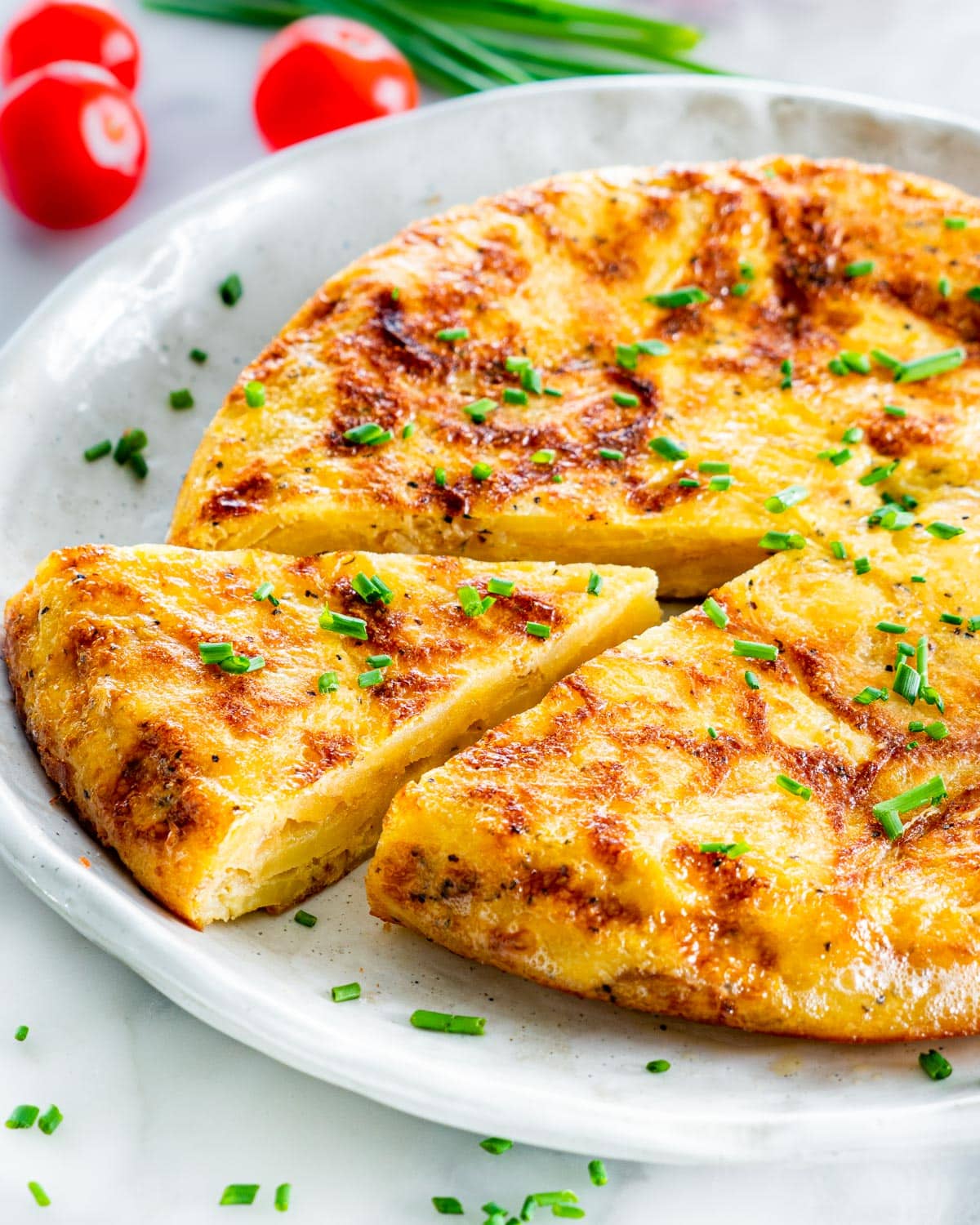 Side view of Spanish tortilla on a plate with one slice cut out and garnished with chives