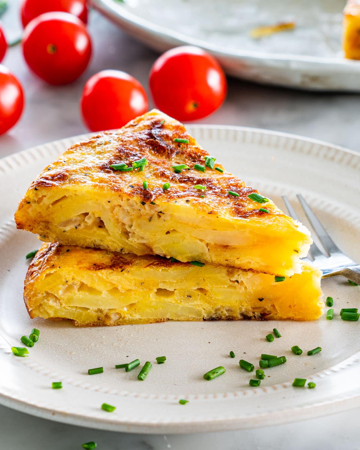 two slices of Spanish tortilla stacked on top of each other on a beige plate garnished with chives