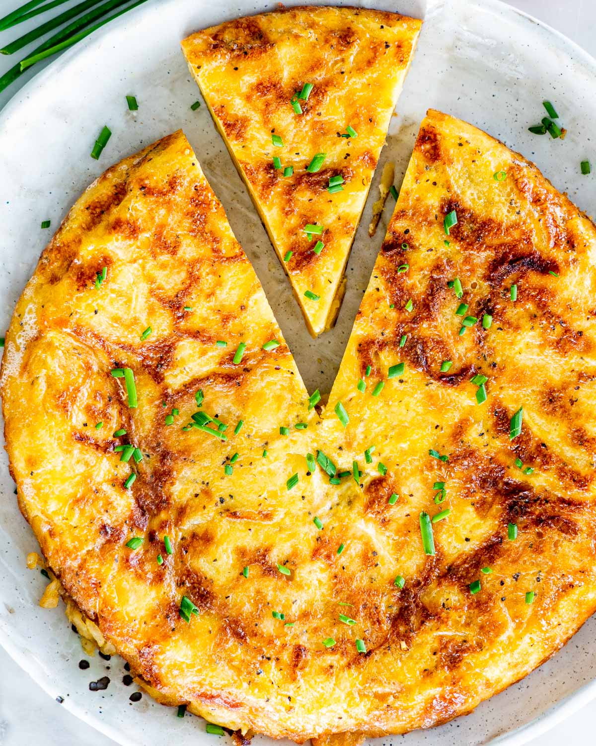 Overhead shot of Spanish tortilla on a plate with one slice cut out and garnished with chives