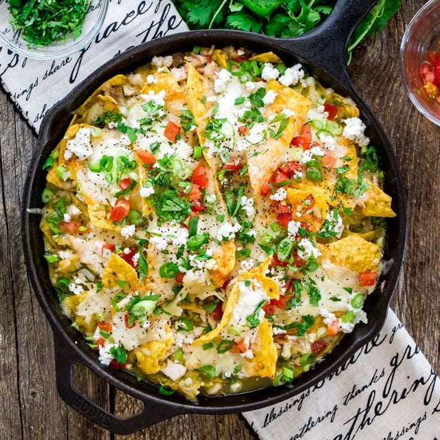 atop a skillet filled with chilaquiles and topped with queso fresco, tomatoes, parsley, and scallions