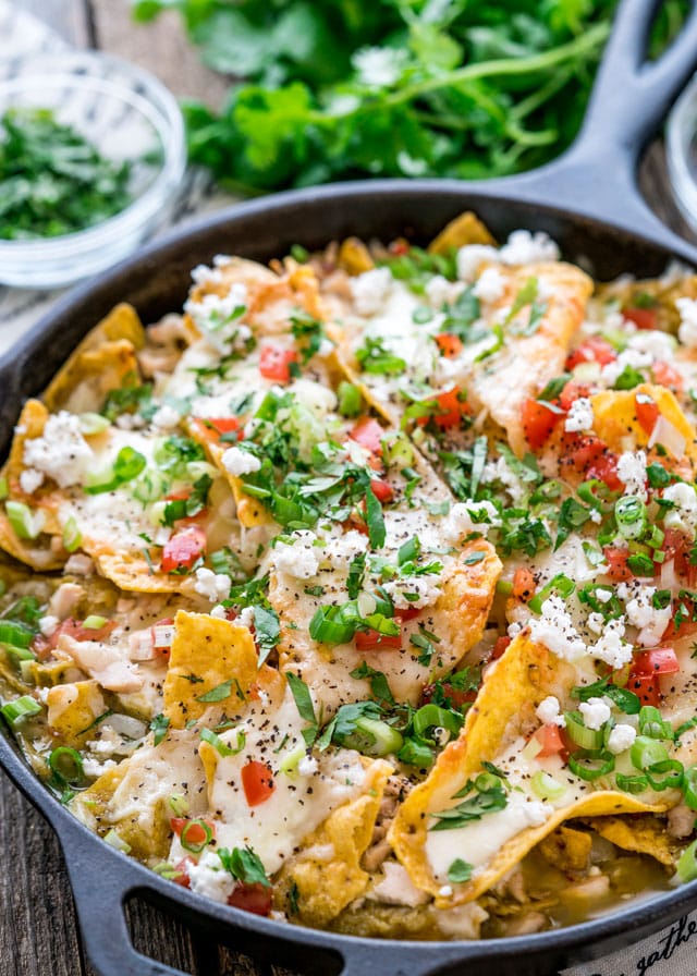 a skillet filled with chilaquiles and topped with queso fresco, parsley, parsley and chives