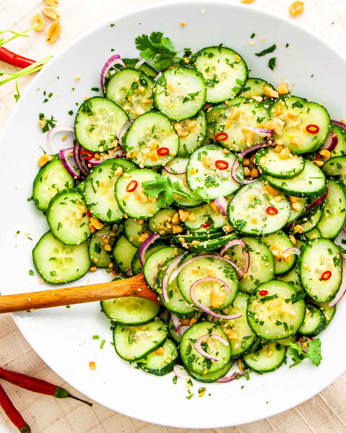 Overhead shot of freshly made Thai cucumber salad on a white plate with a wooden spoon inside