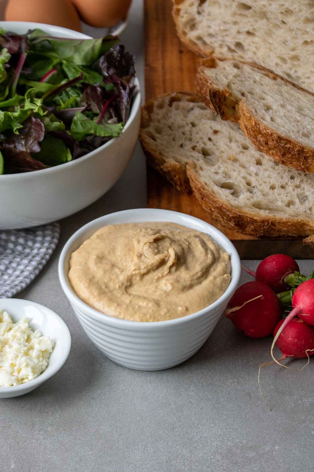 Ingredients for hummus bowls; hummus, feta cheese, leafy greens, radishes, and sourdough bread.