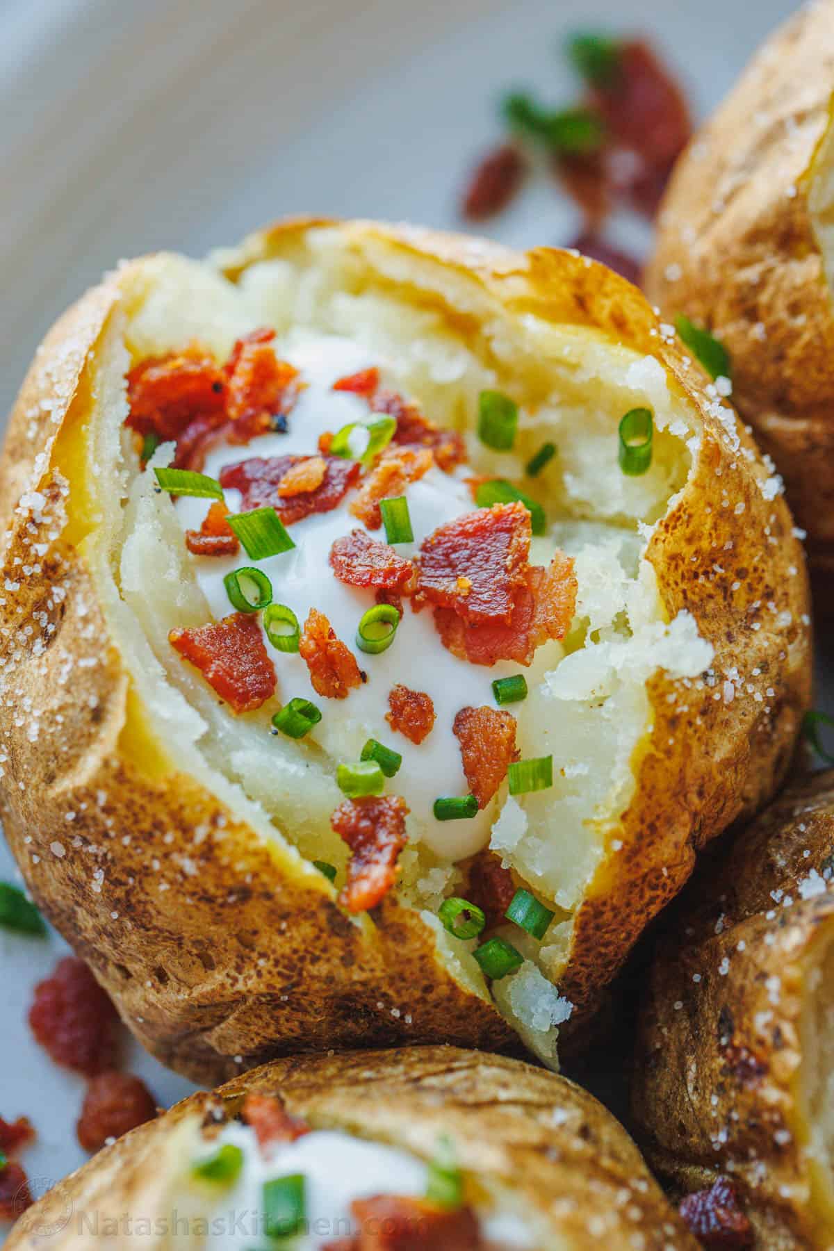 Close up view of a perfect baked potato topped with sour cream, bacon, and chives.