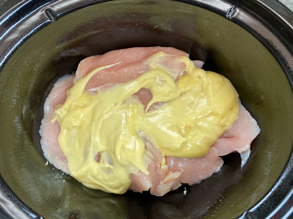 Raw chicken breast and chicken soup in a Crock Pot.