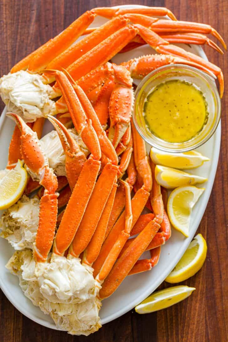 Cooked Crab legs on a serving platter with butter dipping sauce and lemon wedges