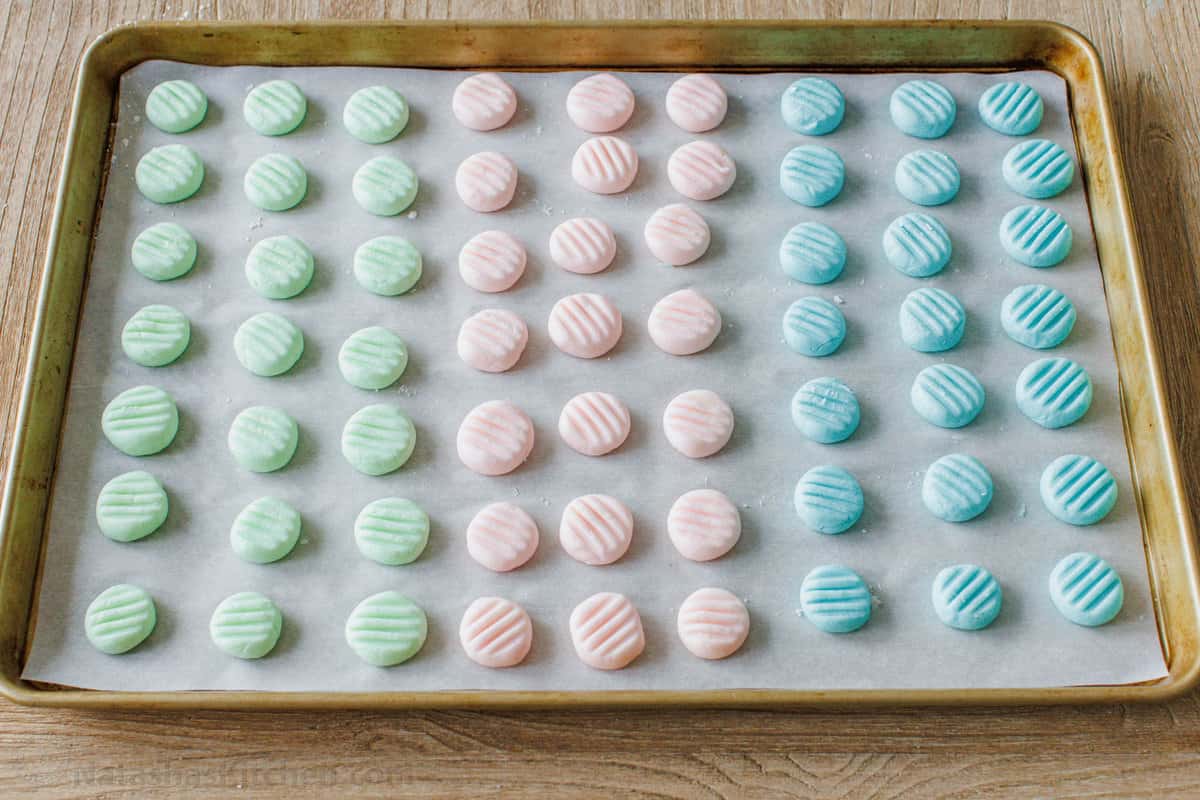 Rows of green, pink, and blue cream cheese mints on a parchment-lined baking sheet.