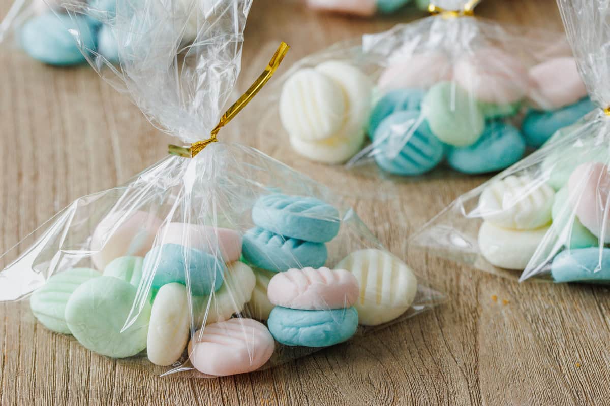 Assorted blue, pink, green, and white cream cheese mints wrapped in small plastic baggies closed with twist-ties.