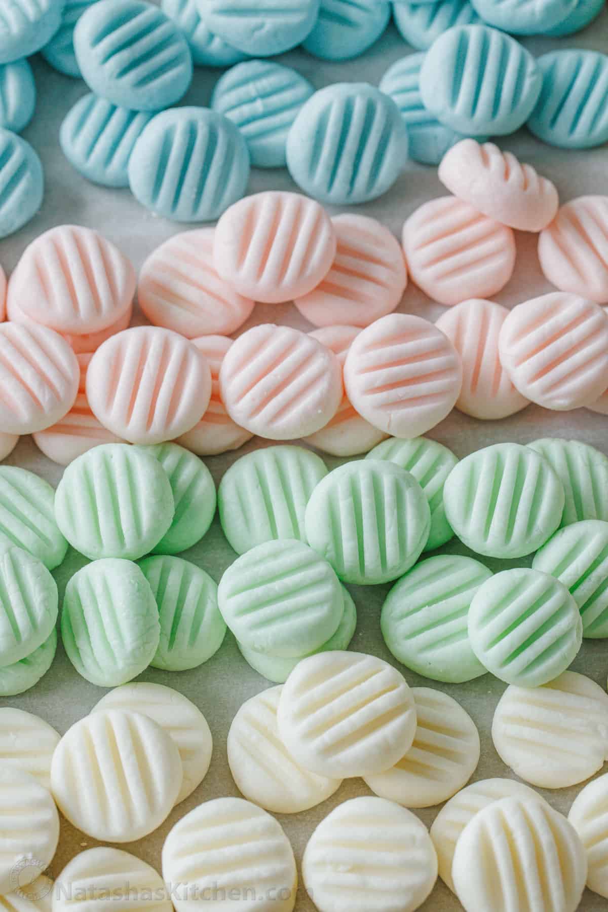 Assorted blue, pink, green, and white cream cheese mints grouped together on a parchment-lined baking sheet.