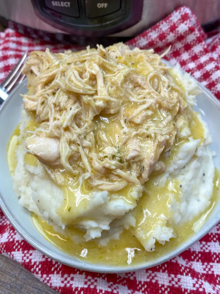 Crockpot chicken with gravy and mashed potatoes on a white plate.