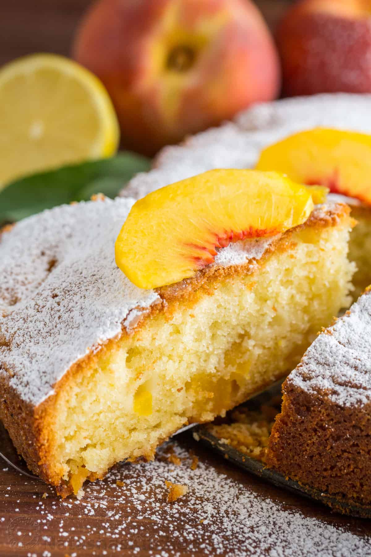 Slice of summer peach cake dusted with confectioners' sugar and topped with fresh sliced peach
