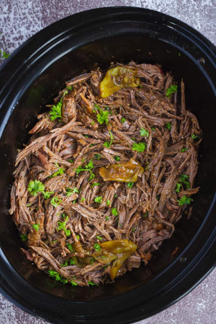 Shredded Mississippi Roast in a slow cooker topped with garnish.