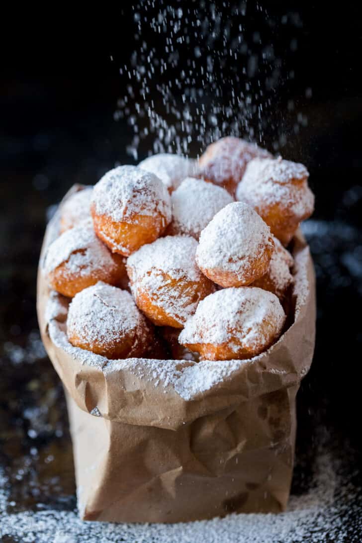 Zeppole in paper bag dusted with powdered sugar. 