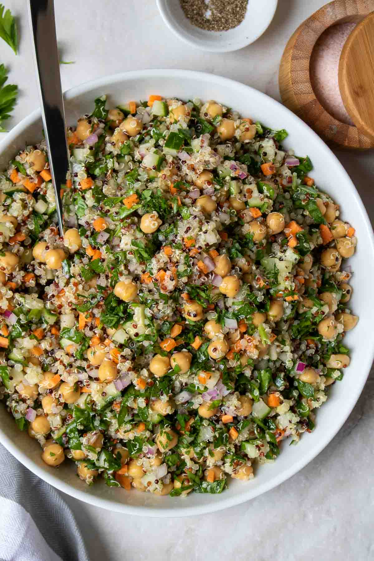 Quinoa chickpea salad in a white bowl with a silver spoon and a side of salt and pepper.