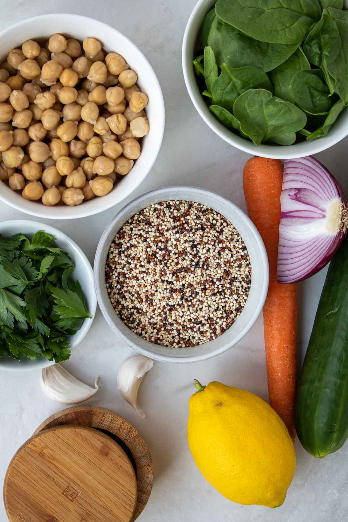 Ingredients for quinoa chickpea salad: canned chickpeas, quinoa, cucumber, carrot, red onion, spinach, parsley, olive oil, lemon, garlic, salt, and pepper.
