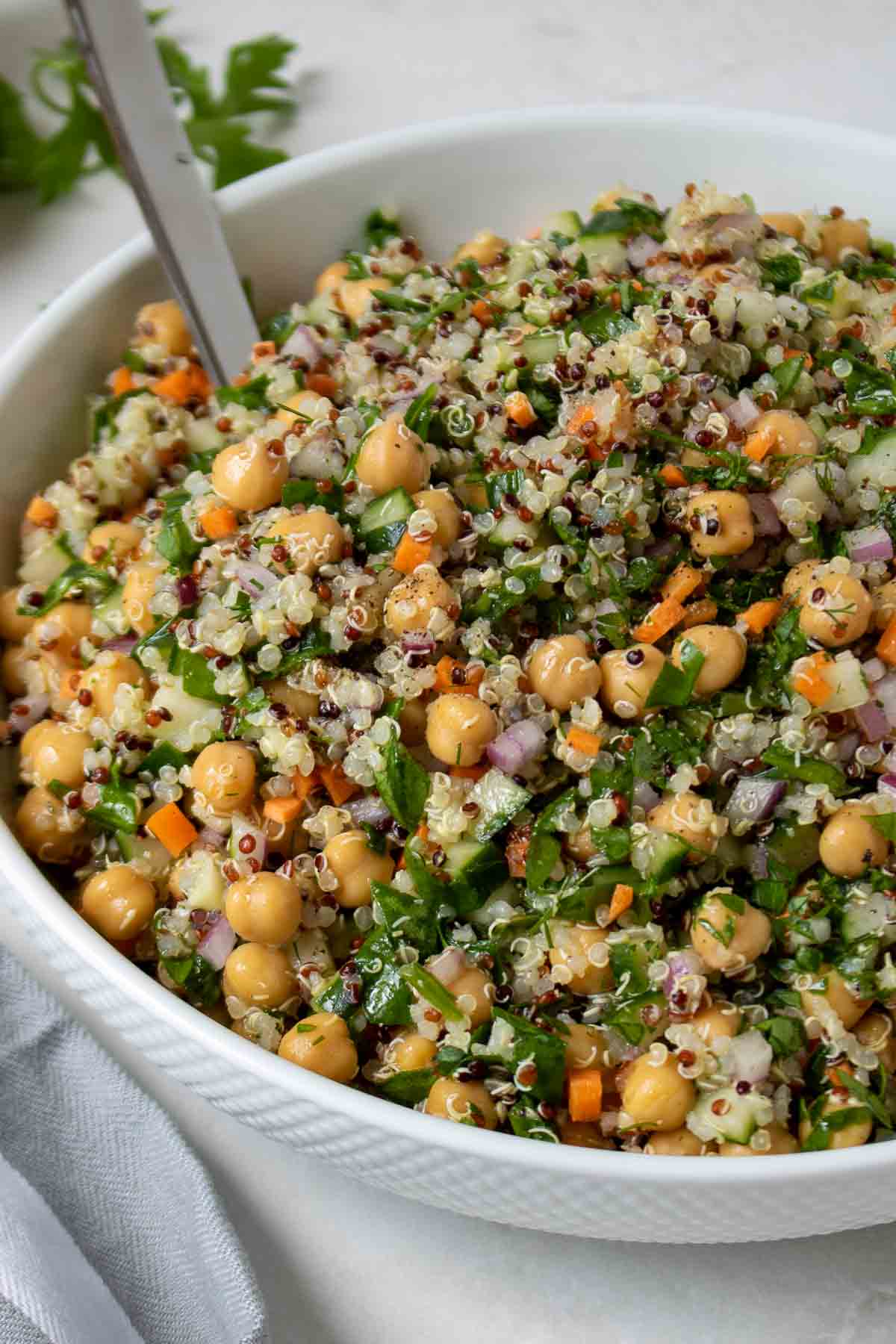 Close up of lemon quinoa chickpea salad in a white serving bowl with a silver spoon.