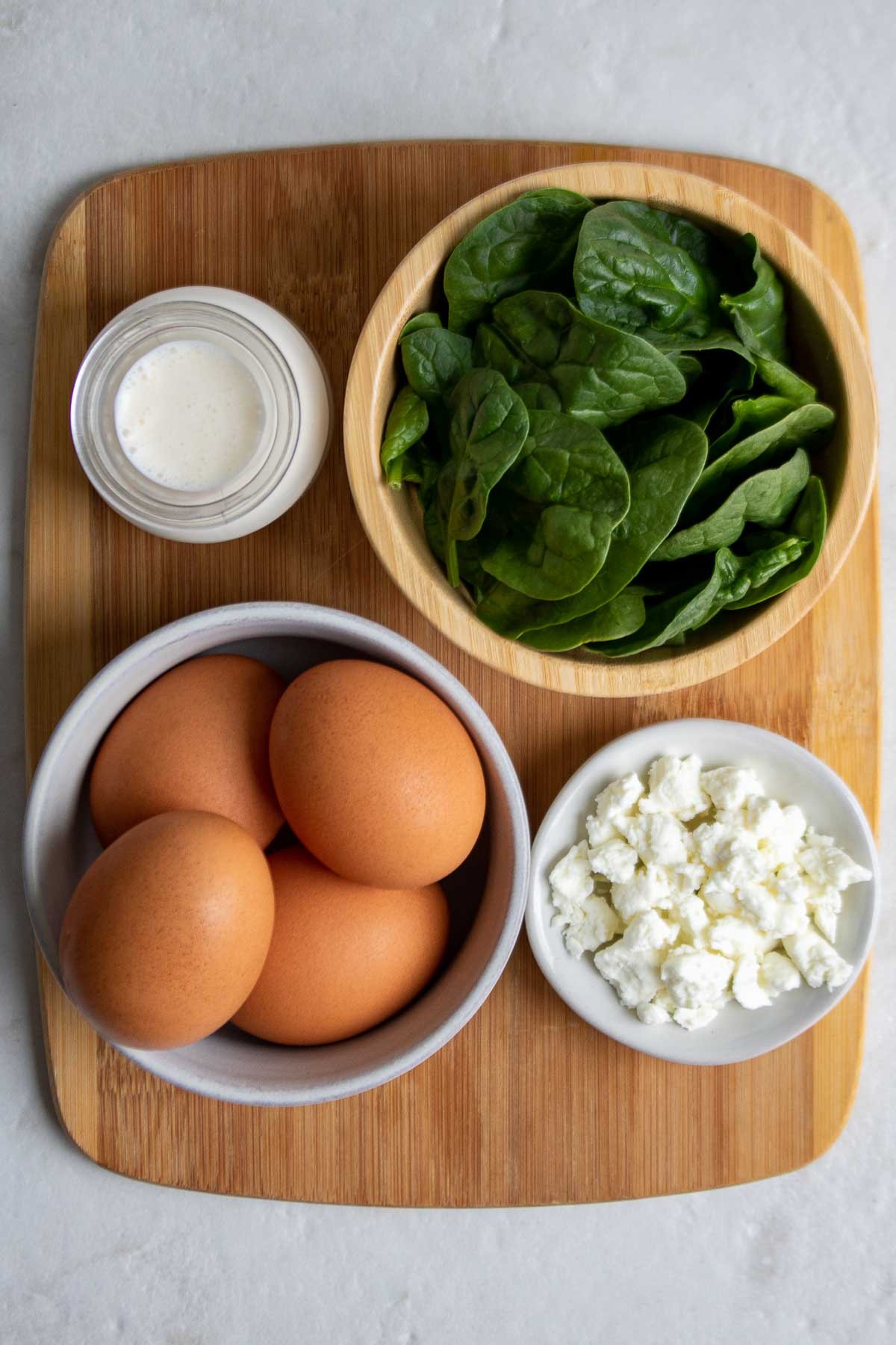 Ingredients for spinach baked eggs; eggs, spinach, heavy cream, and goat cheese.