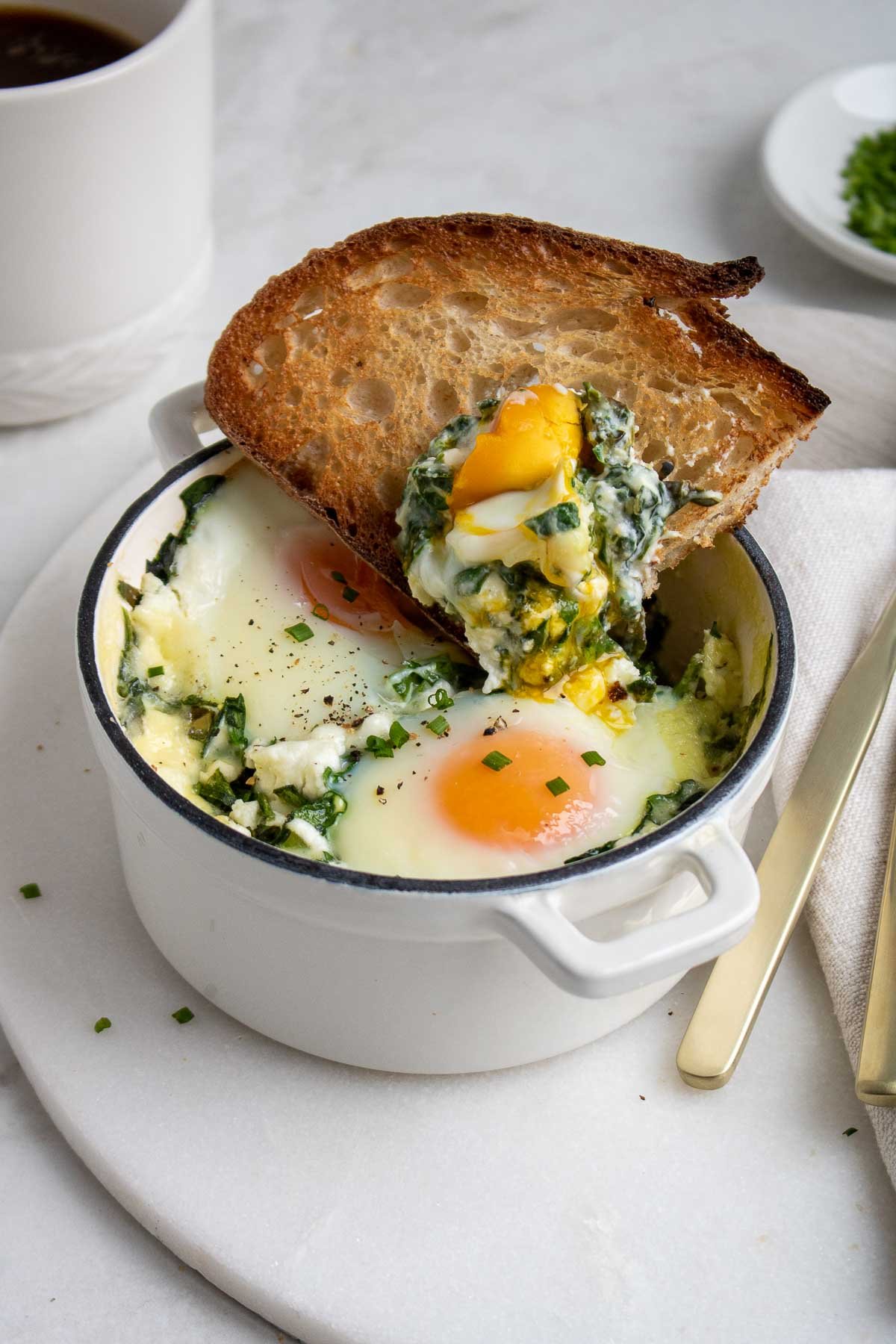 Close of creamy spinach baked eggs with a slice of toast dunked into it.