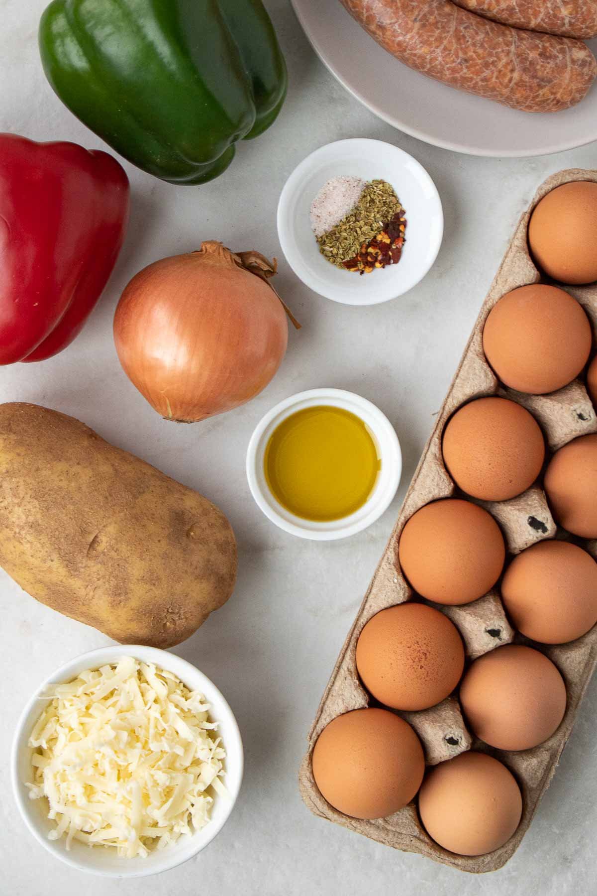 Ingrédients pour la casserole de petit-déjeuner : œufs, saucisses, pommes de terre, poivron rouge, poivron vert, oignon, origan, flocons de piment rouge, sel, huile d'olive, fromage cheddar