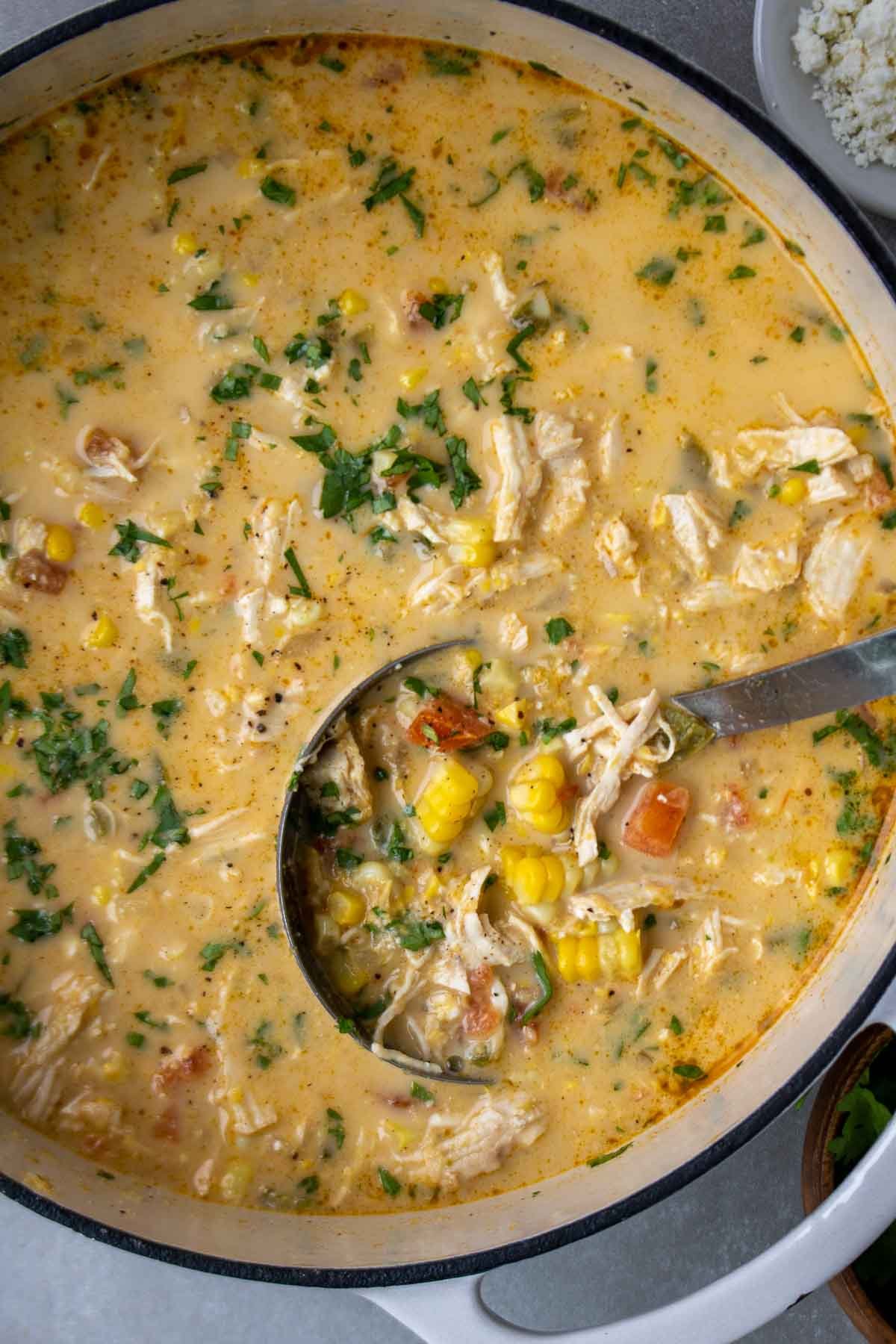Mexican sweet corn soup with chicken in a large pot with a ladle and chopped cilantro on top.