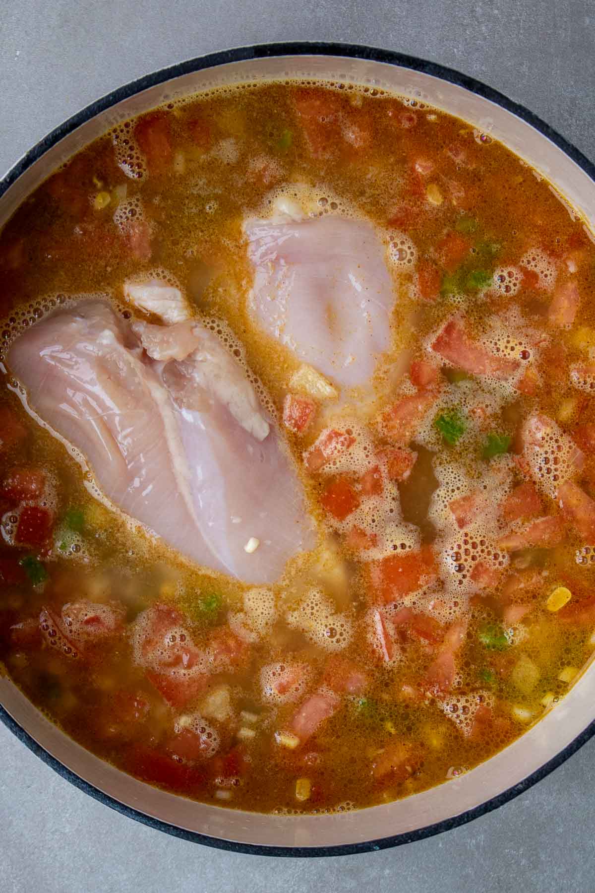 Légumes pour la soupe au maïs au poulet dans une marmite avec du bouillon de poulet et des blancs de poulet crus.