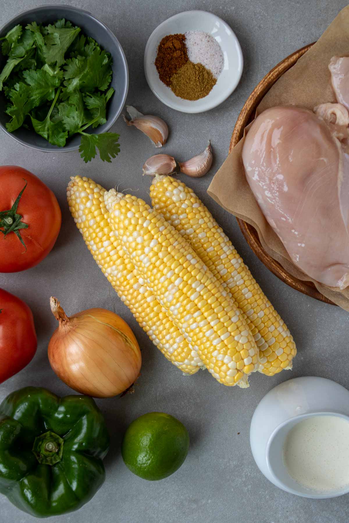 Ingredients for Mexican corn chicken soup; chicken breasts, fresh sweet corn, tomatoes, onion, garlic, green bell pepper, cilantro, cumin, chili powder, salt, and heavy cream.