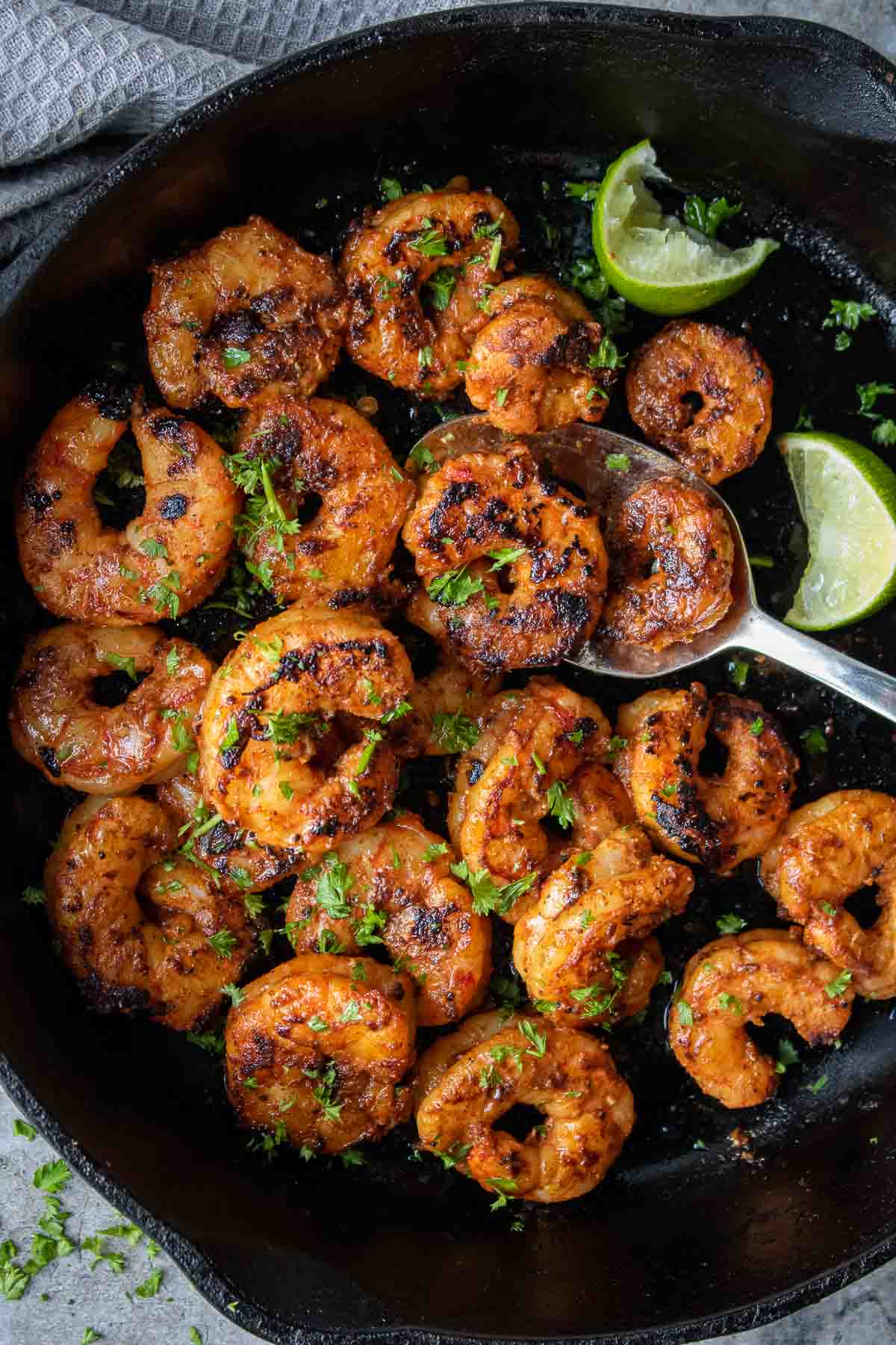 Blackened shrimp in a cast iron pan with fresh cilantro on top and lime wedges on the side.