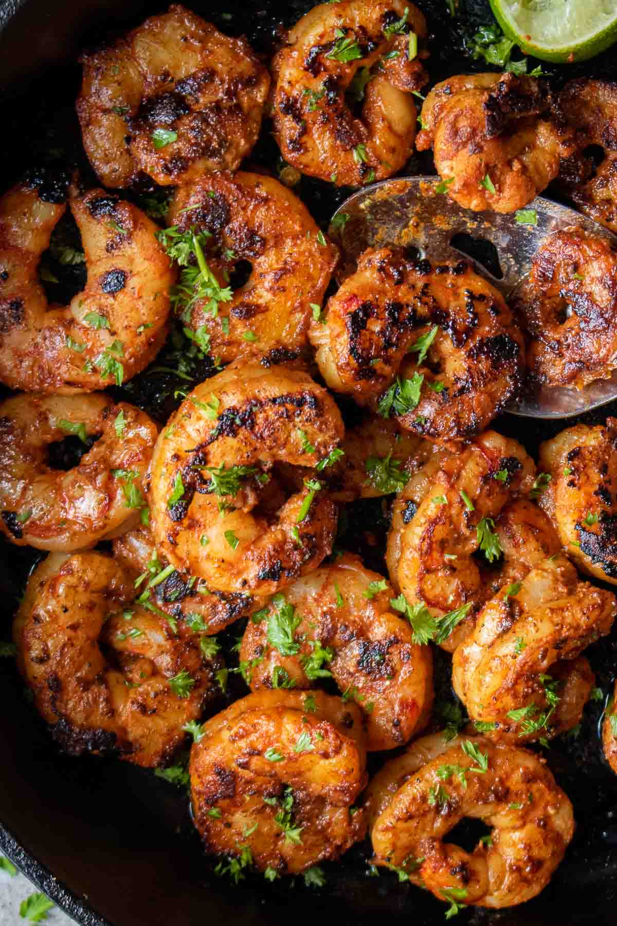 Close up of cooked blackened shrimp in a cast iron pan on a spoon.