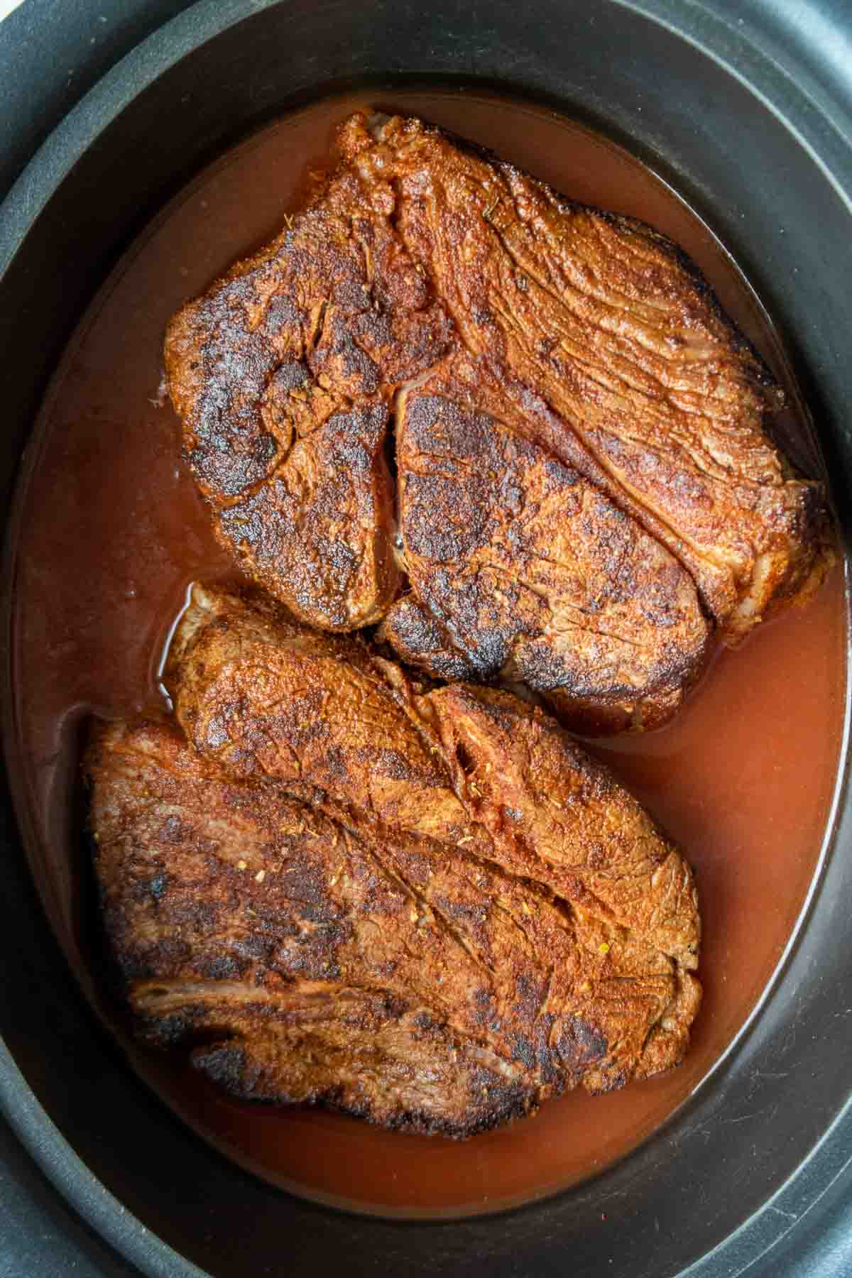 Seared beef chuck roast in a slow cooker with broth and tomato paste.
