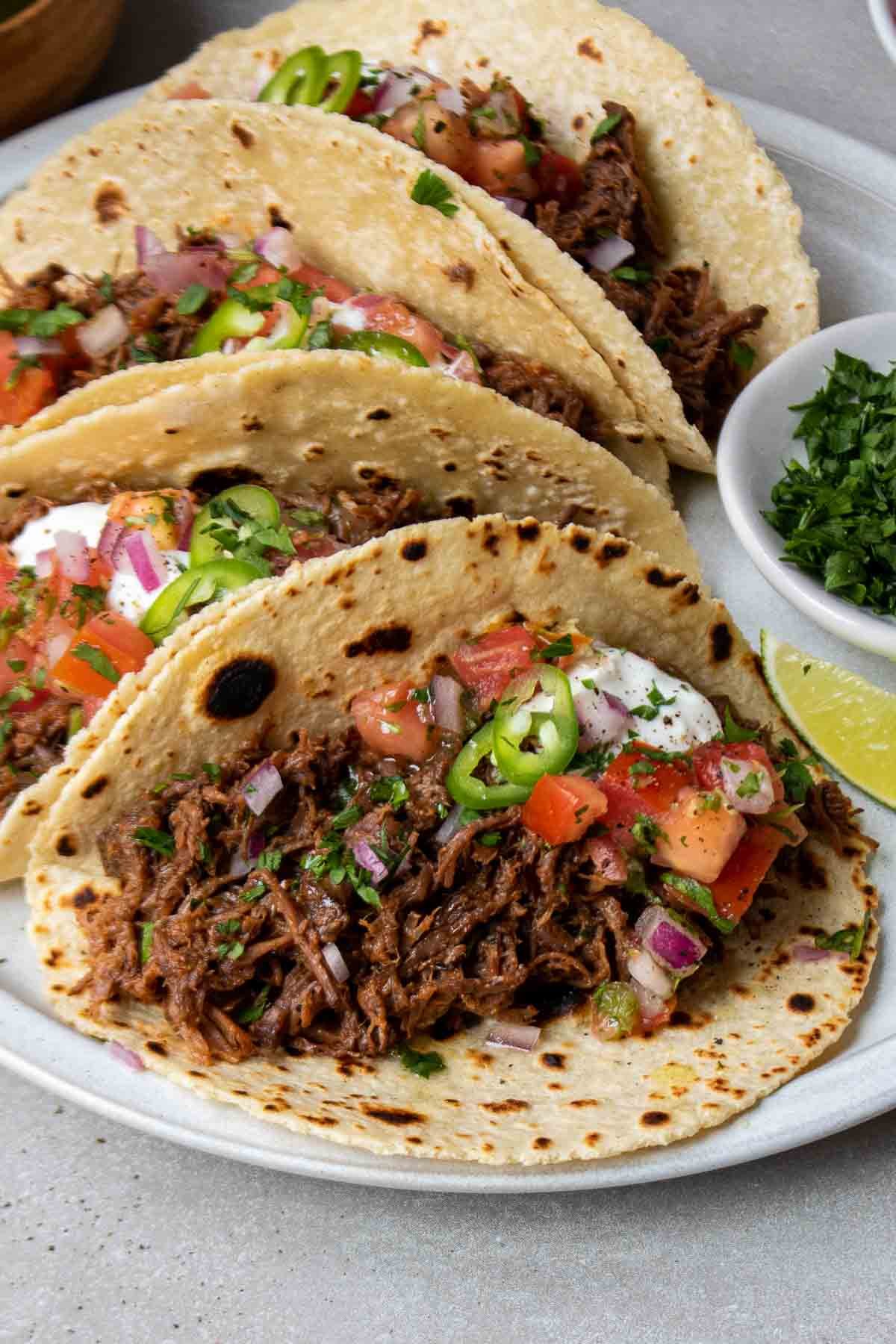 Mexican shredded beef tacos on a plate with toppings.