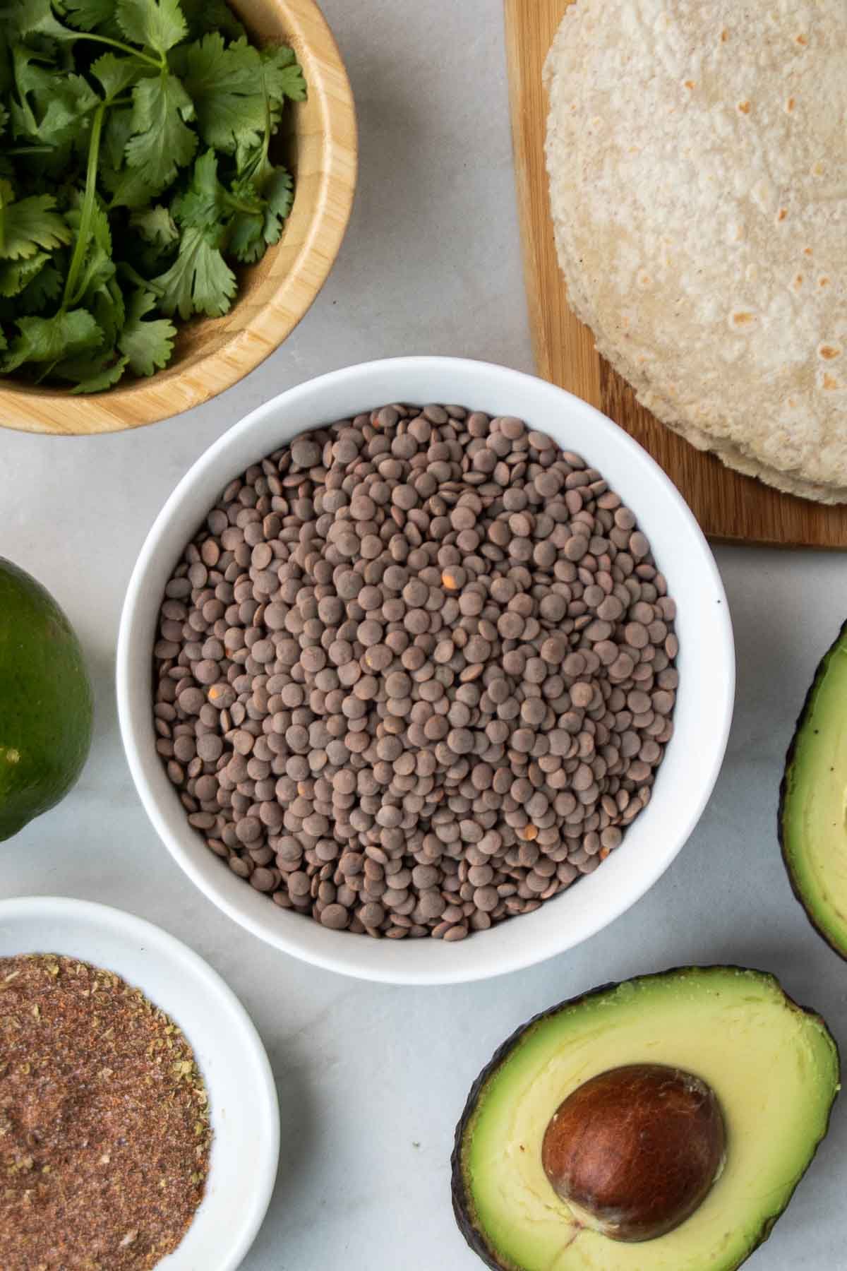 Ingredients for lentil taco meat: brown lentils, homemade taco seasoning, tortillas, avocado, limes, and cilantro.
