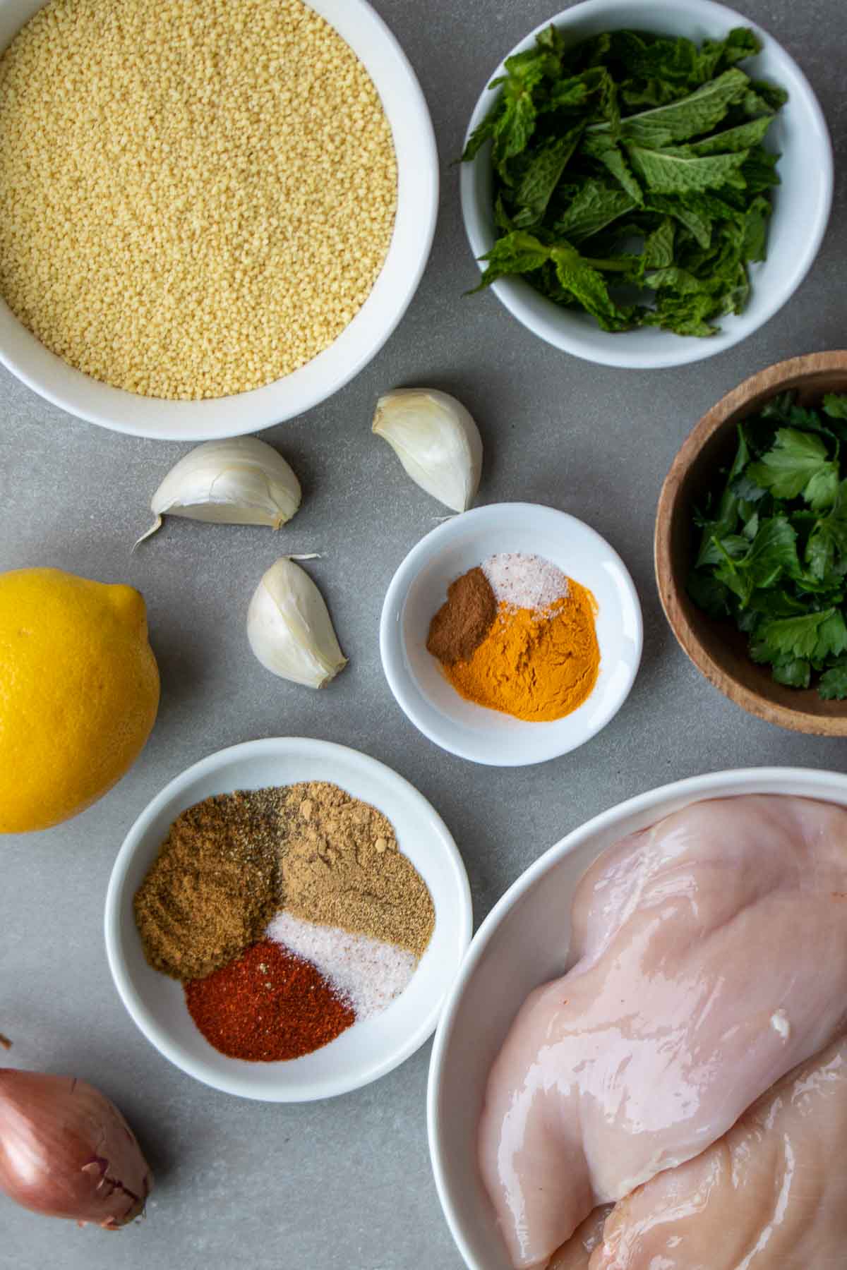Ingredients for a chicken and couscous recipe including chicken breasts, couscous, garlic, shallot, paprika, cumin, coriander, salt, turmeric, cinnamon, lemon, mint, and parsley