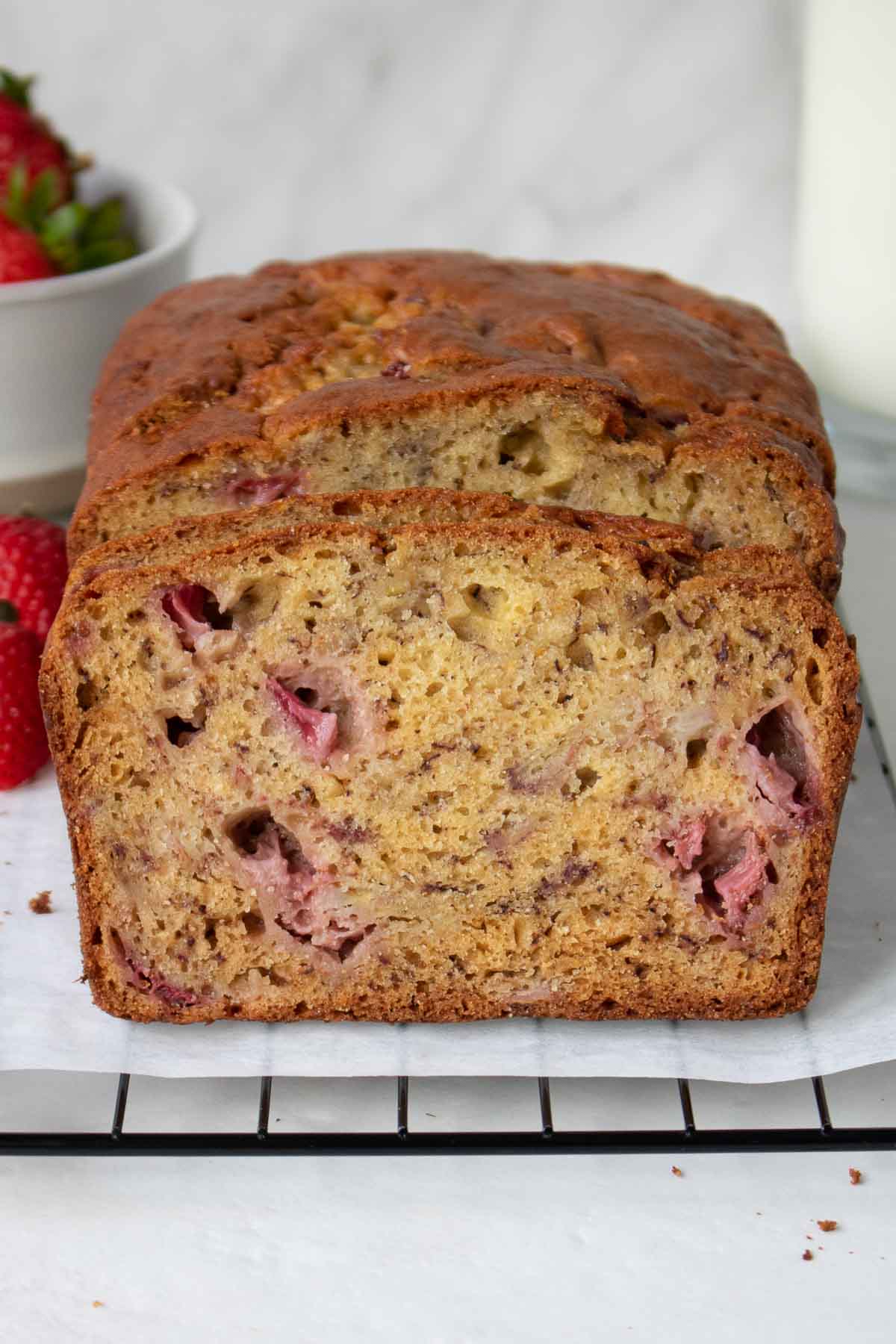 Close-up of banana bread with strawberries on a baking rack.