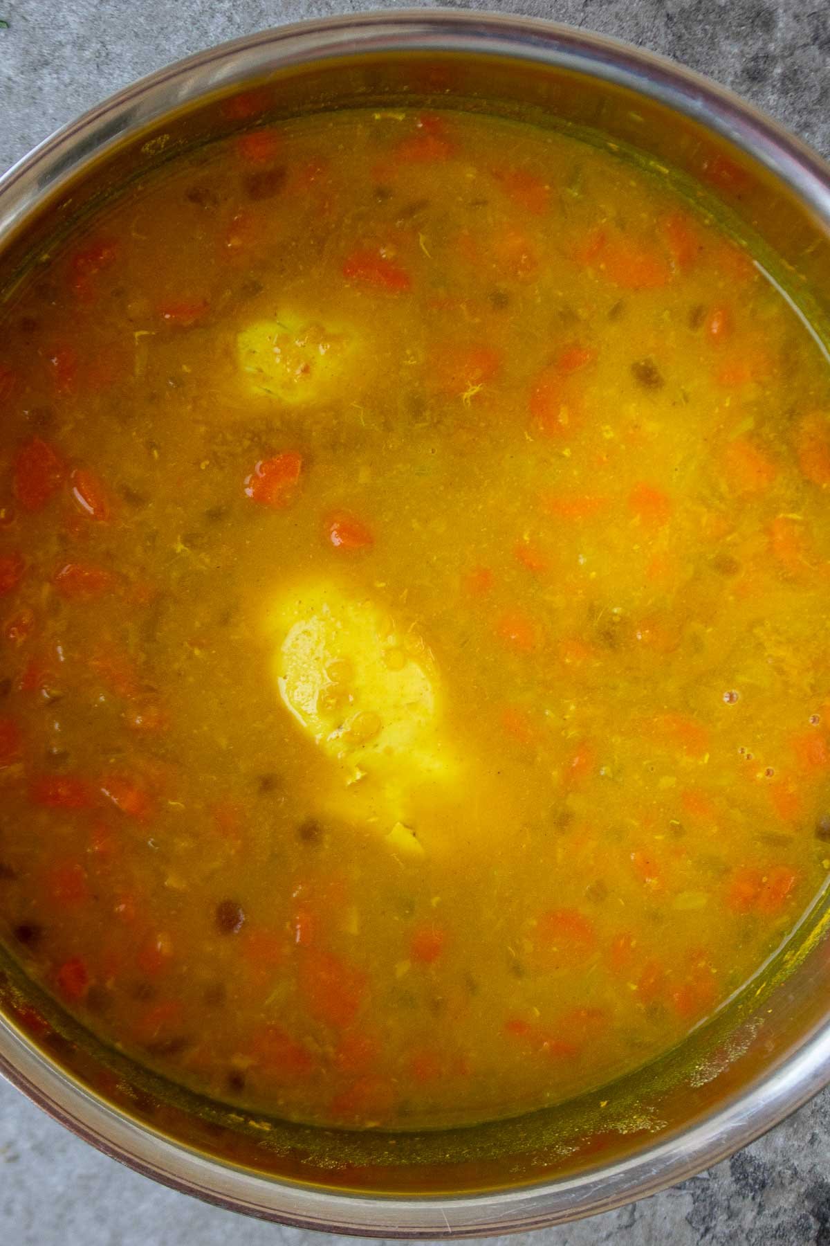 Large pot with soup with cooked red lentils and chicken.